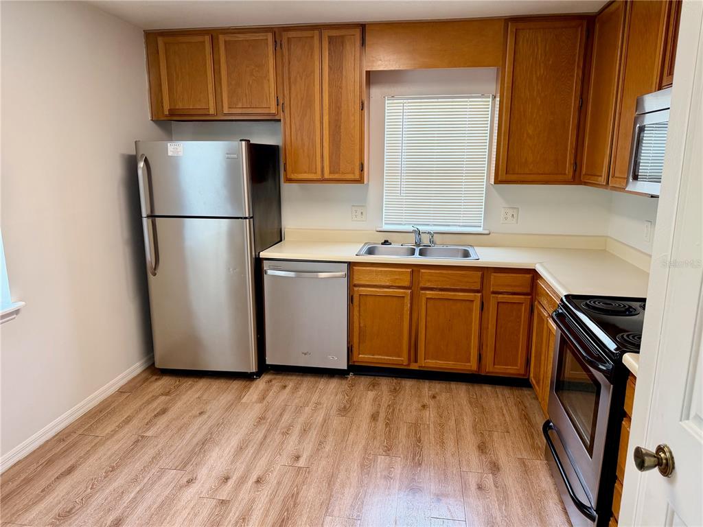 A kitchen with wood cabinets, stainless steel appliances, a double sink, and wood-look flooring — 4316 CLUBSIDE DRIVE UNIT 4316, LONGWOOD, FL
