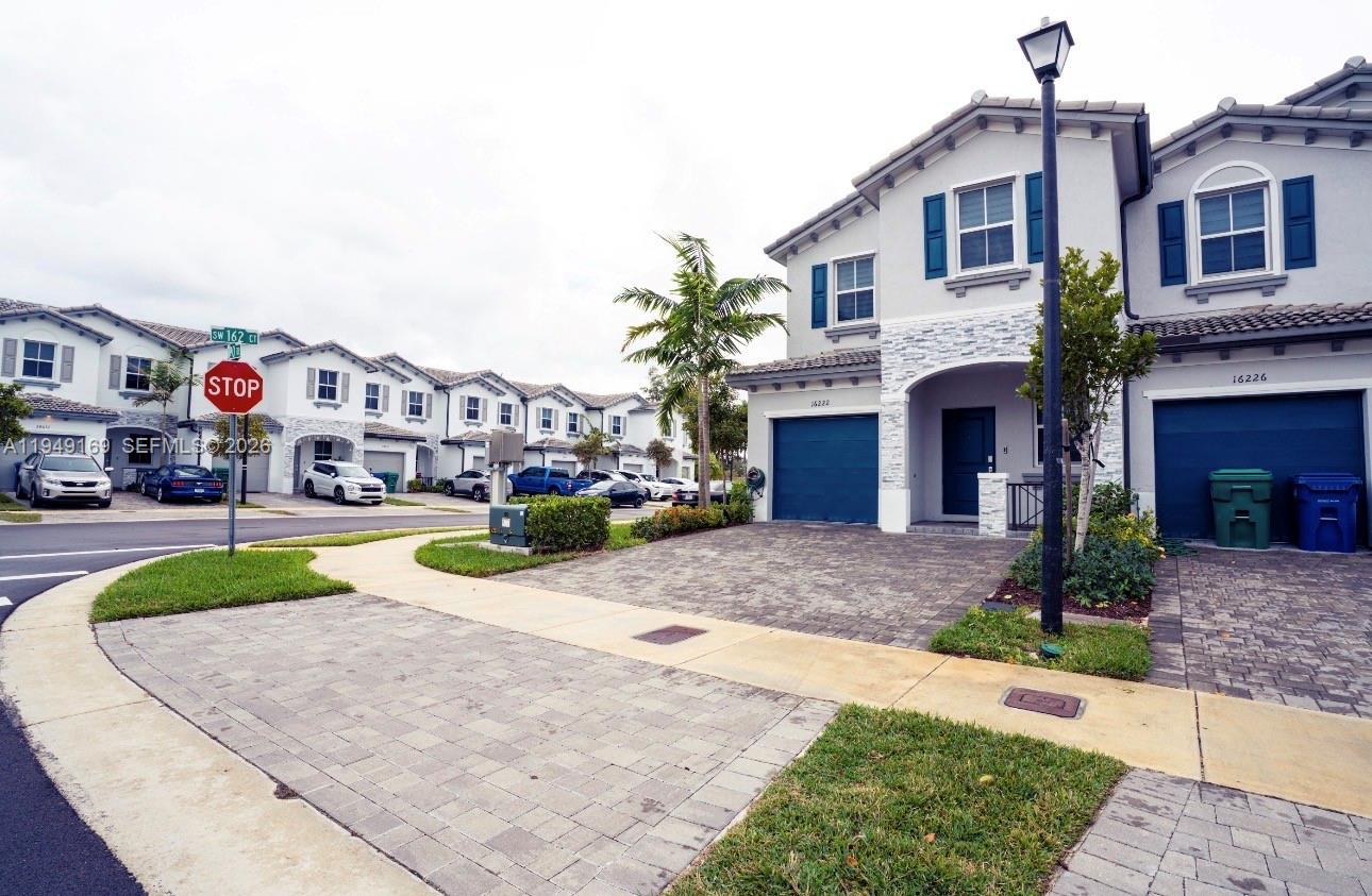 A street-level view of two-story townhomes with paved driveways and a stop sign — 16222 SW 290th Ter, Homestead FL 33033, HOMESTEAD, FL