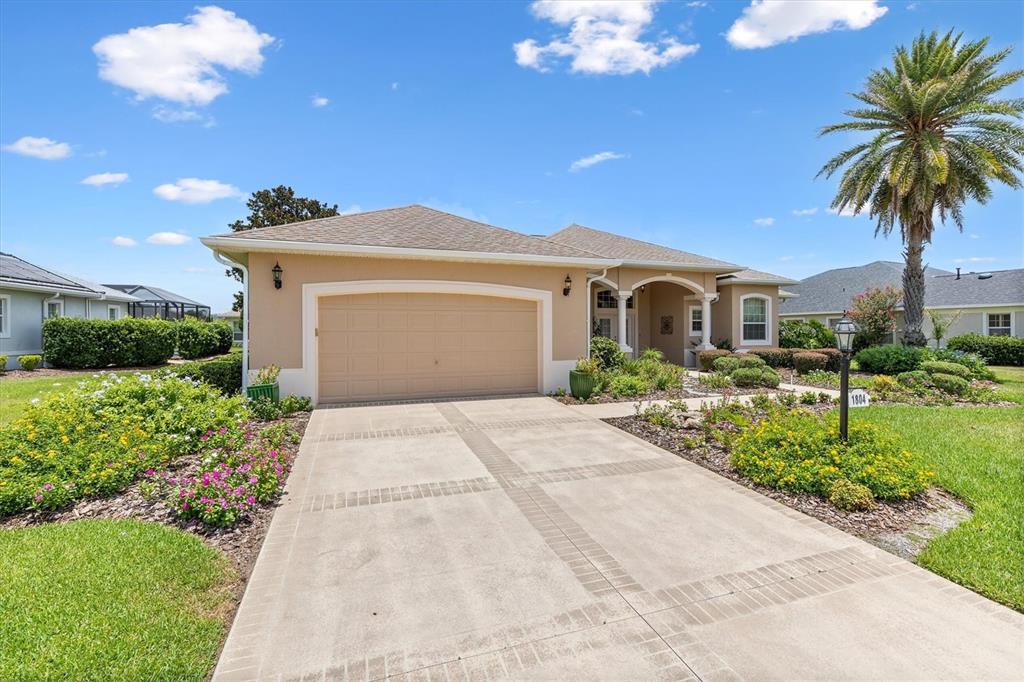 A beige single-story house features a two-car garage, a paved driveway, and a palm tree — 1804 SUNSET RIDGE DRIVE, THE VILLAGES, FL