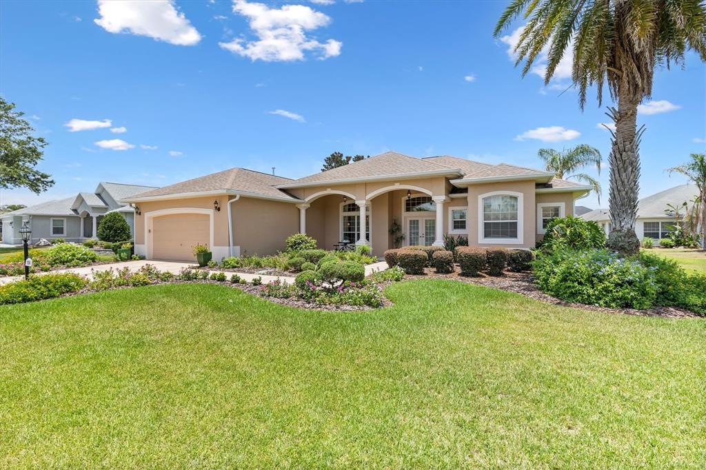 A single-story house with a beige stucco exterior, a two-car garage, and a palm tree — 1804 SUNSET RIDGE DRIVE, THE VILLAGES, FL