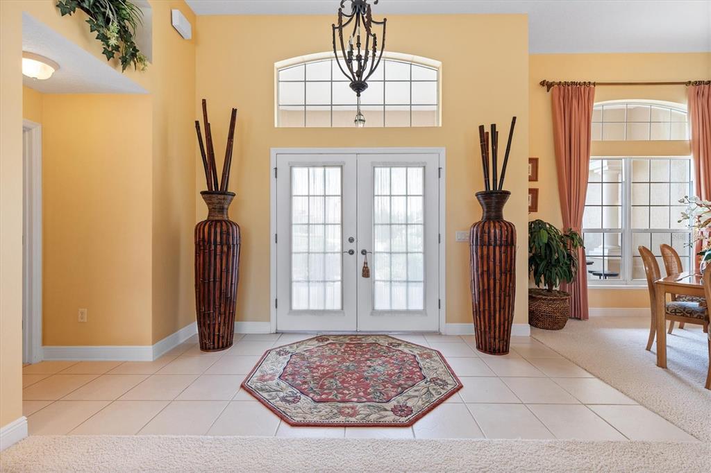 A foyer with tile flooring, an octagonal rug, tall decorative vases, and double glass doors — 1804 SUNSET RIDGE DRIVE, THE VILLAGES, FL