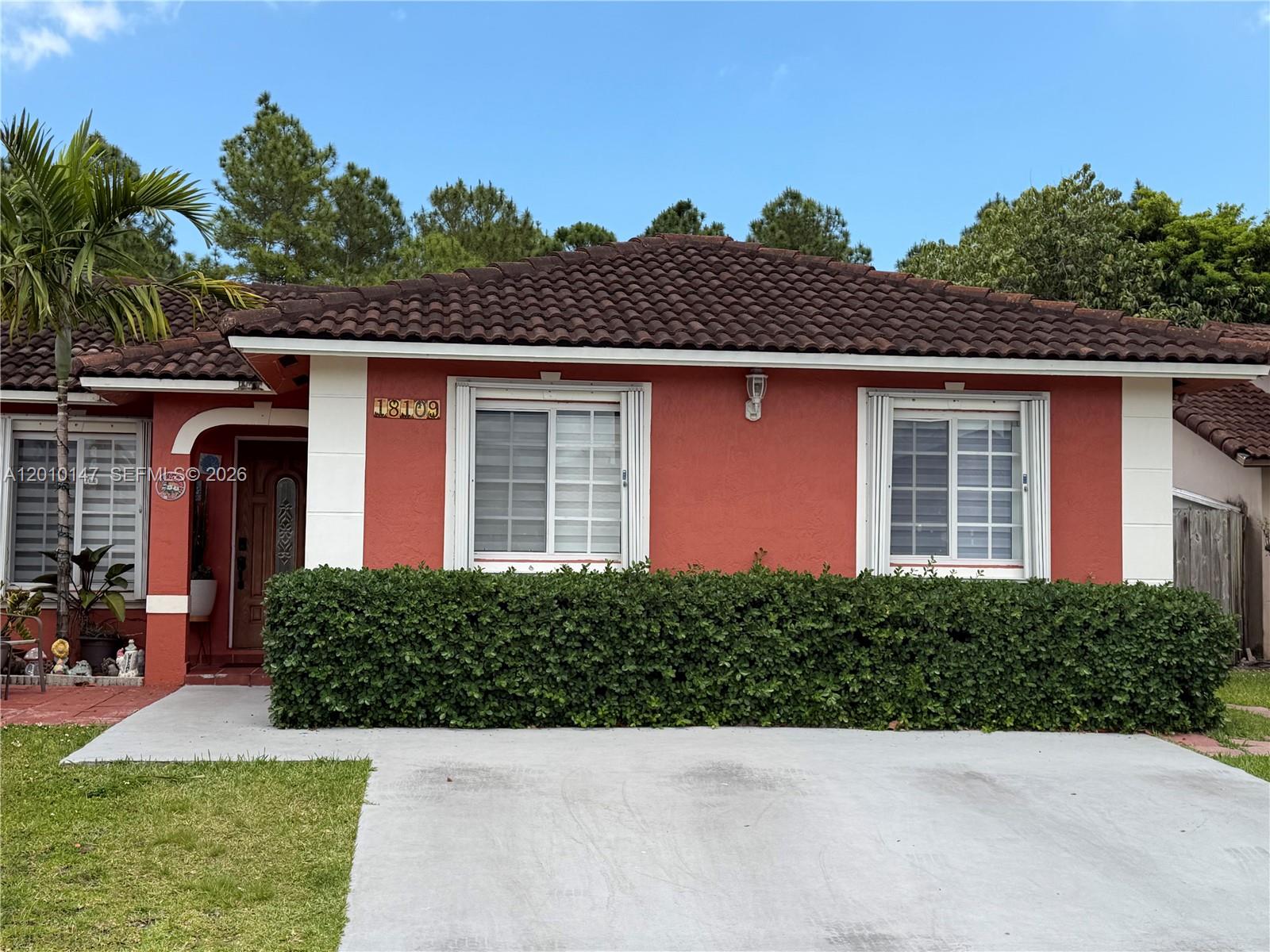 A single-story house with a red stucco exterior, a tiled roof, and a front hedge — 18109 SW 142nd Ct, Miami FL 33177, MIAMI, FL