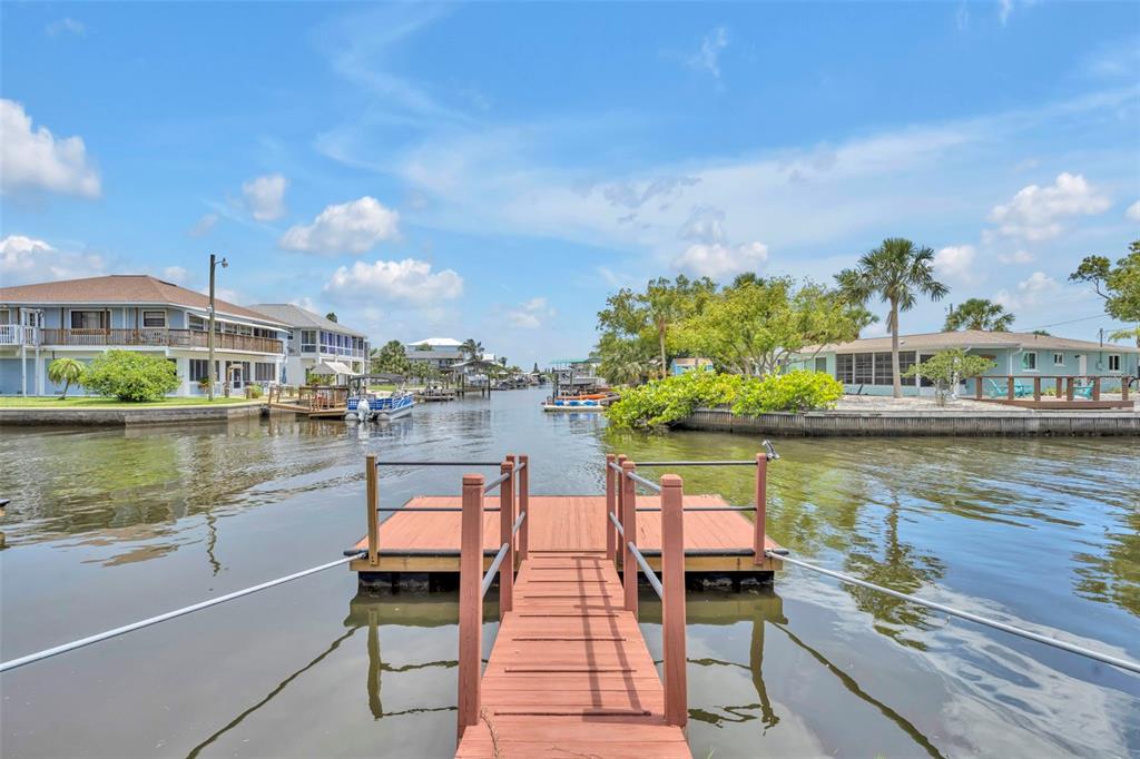 A wooden dock extends into a canal surrounded by waterfront houses under a blue sky — 6416 BOATYARD DRIVE, HUDSON, FL