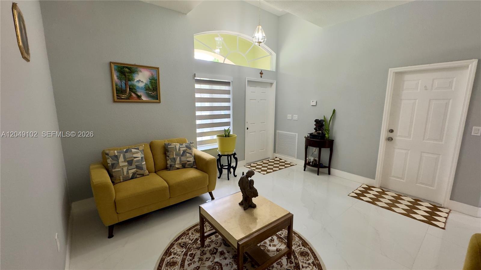 A bright living room features a yellow sofa, marble floors, and a high vaulted ceiling — 937 NE 35th Ave, Homestead FL 33033, HOMESTEAD, FL