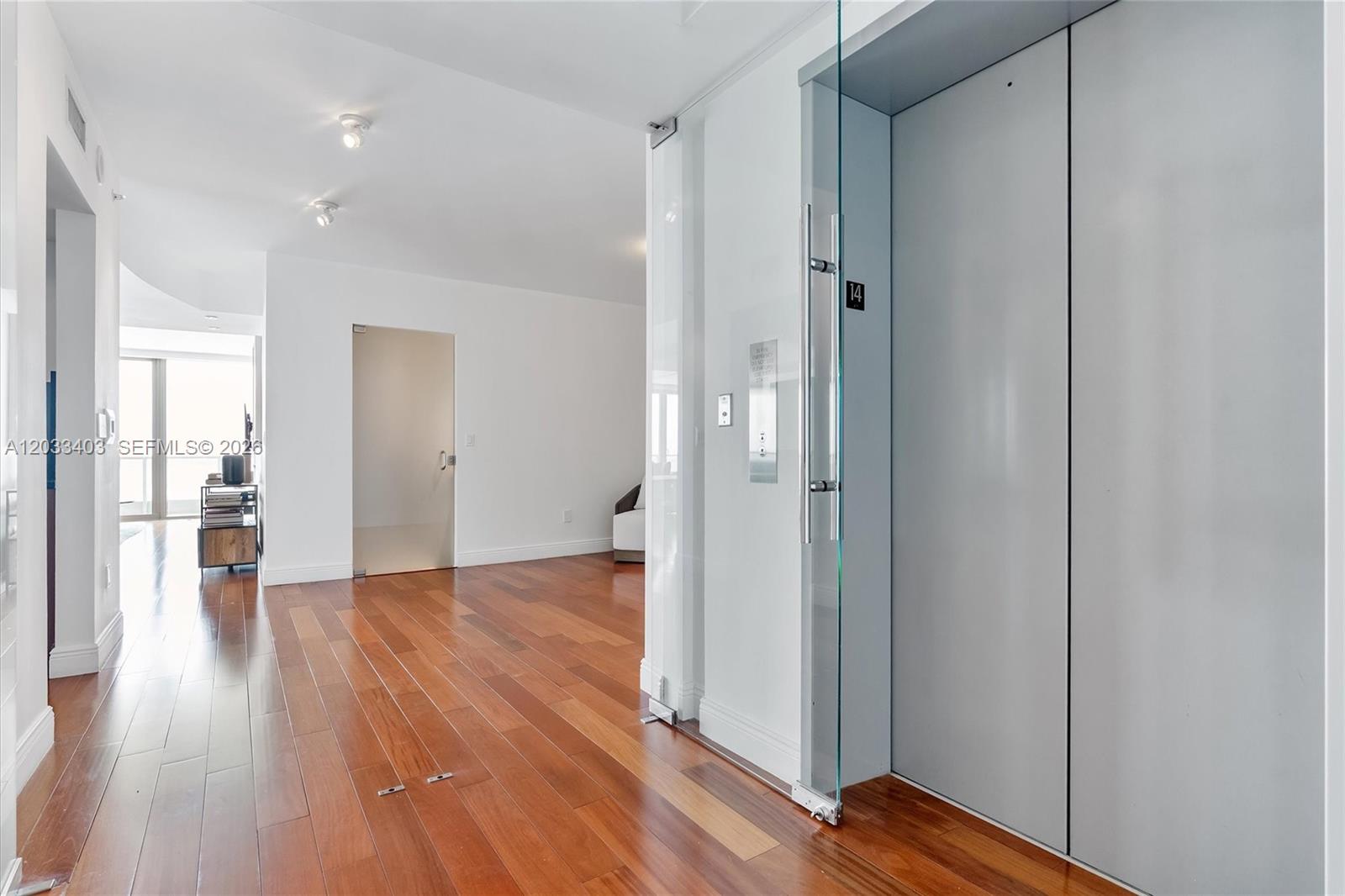 A modern interior features hardwood floors, white walls, and a private glass-enclosed elevator entrance — 1331 Brickell Bay Dr # 1409, Miami FL 33131, MIAMI, FL