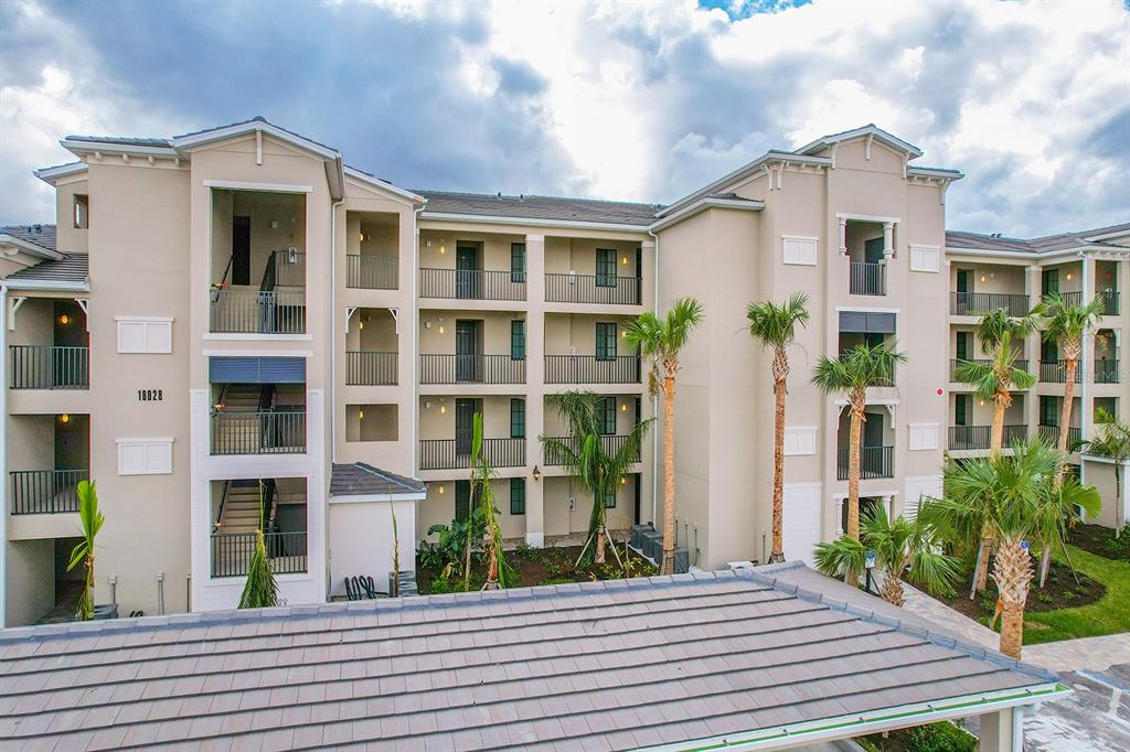 A multi-story apartment building exterior features tan stucco walls, dark railings, and palm trees — 18028 GAWTHROP DRIVE UNIT 304, BRADENTON, FL