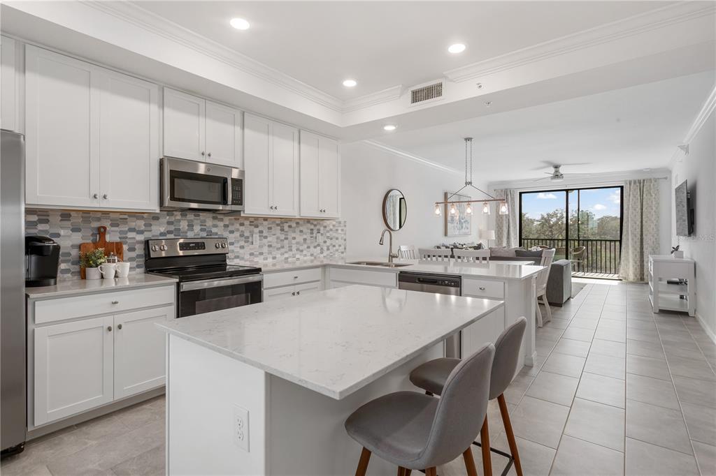 A modern kitchen features white cabinetry, a quartz-topped island, and a tiled backsplash — 18028 GAWTHROP DRIVE UNIT 304, BRADENTON, FL
