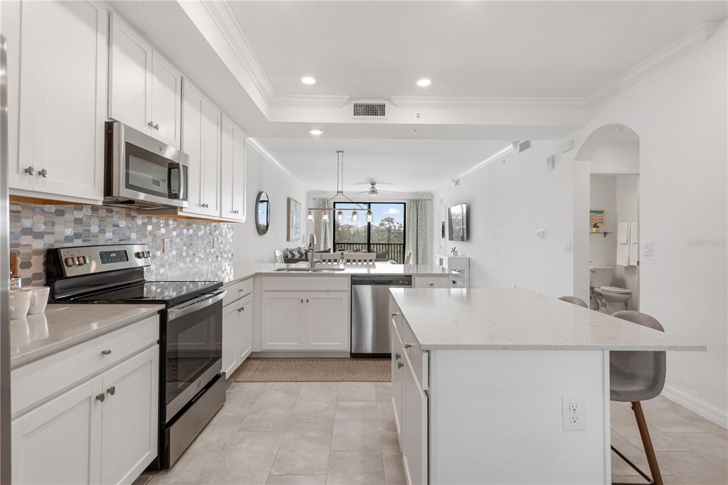 A white kitchen features stainless steel appliances, a quartz island, and a tiled backsplash — 18028 GAWTHROP DRIVE UNIT 304, BRADENTON, FL