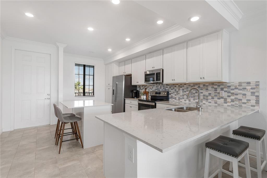 A modern kitchen features white cabinetry, quartz countertops, a tiled backsplash, and a breakfast bar — 18028 GAWTHROP DRIVE UNIT 304, BRADENTON, FL