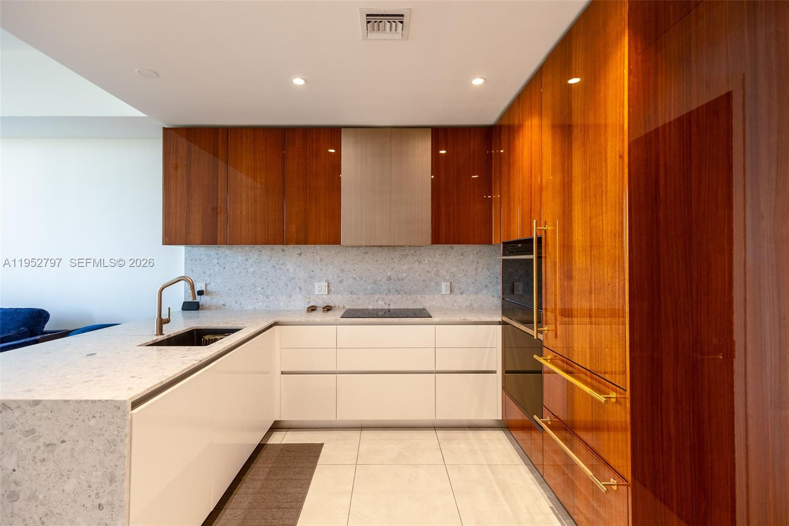 A modern kitchen features white lower cabinets, wood-veneer upper cabinets, and a stone countertop — 2678 Tigertail Ave # 612, Miami FL 33133, MIAMI, FL