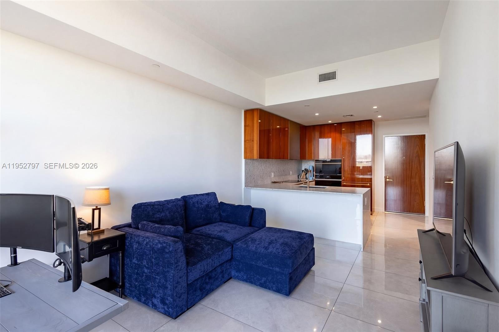 A studio apartment features a blue sofa, a kitchen with wood cabinets, and tile flooring — 2678 Tigertail Ave # 612, Miami FL 33133, MIAMI, FL