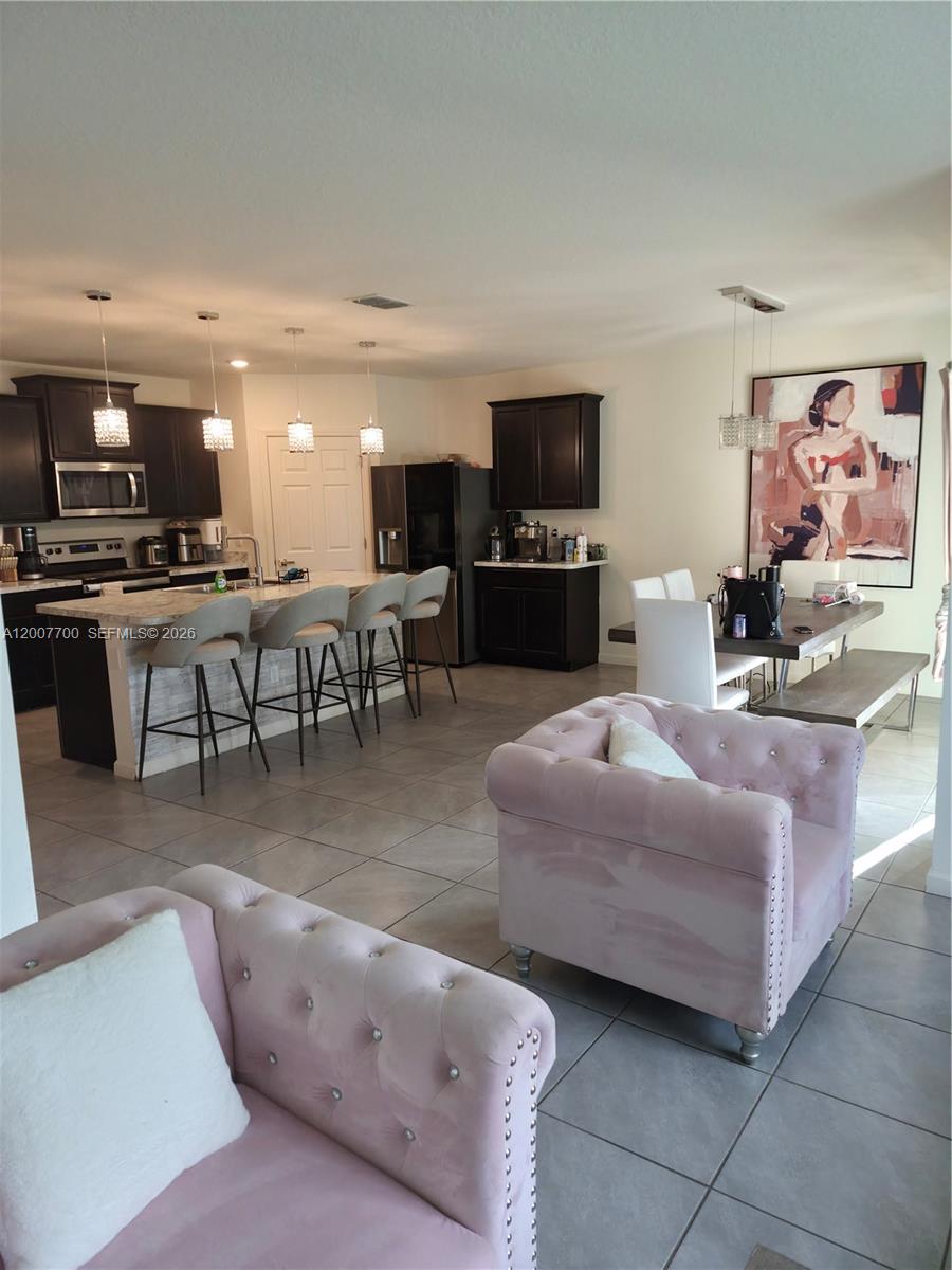 An open-concept kitchen features dark cabinetry, a stone-topped island with bar seating, and dining area — 798 NW Bayshore Blvd, Port St. Lucie FL 34983, PORT ST. LUCIE, FL