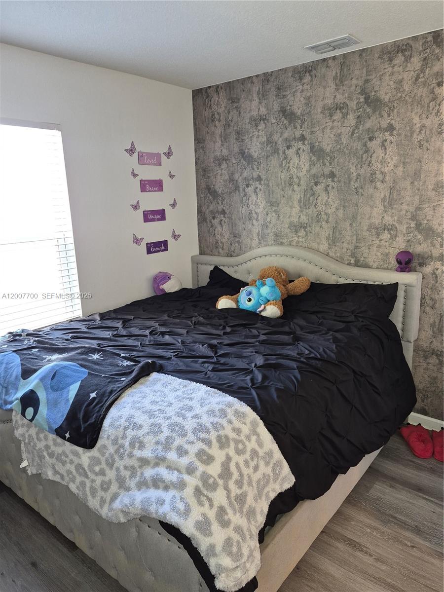 A bedroom features a tufted headboard, a black comforter, and a textured gray accent wall — 798 NW Bayshore Blvd, Port St. Lucie FL 34983, PORT ST. LUCIE, FL