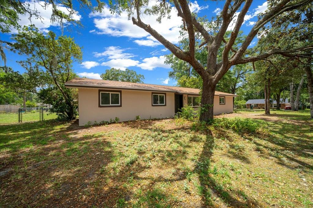 A single-story house with a tan exterior sits on a grassy lot with large trees — 4506 NE 10TH STREET, OCALA, FL