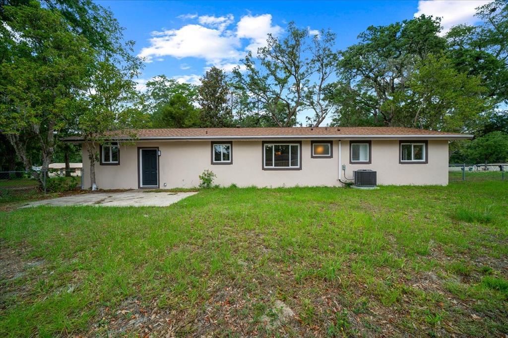 The exterior rear view of a single-story house with a concrete patio and grassy yard — 4506 NE 10TH STREET, OCALA, FL