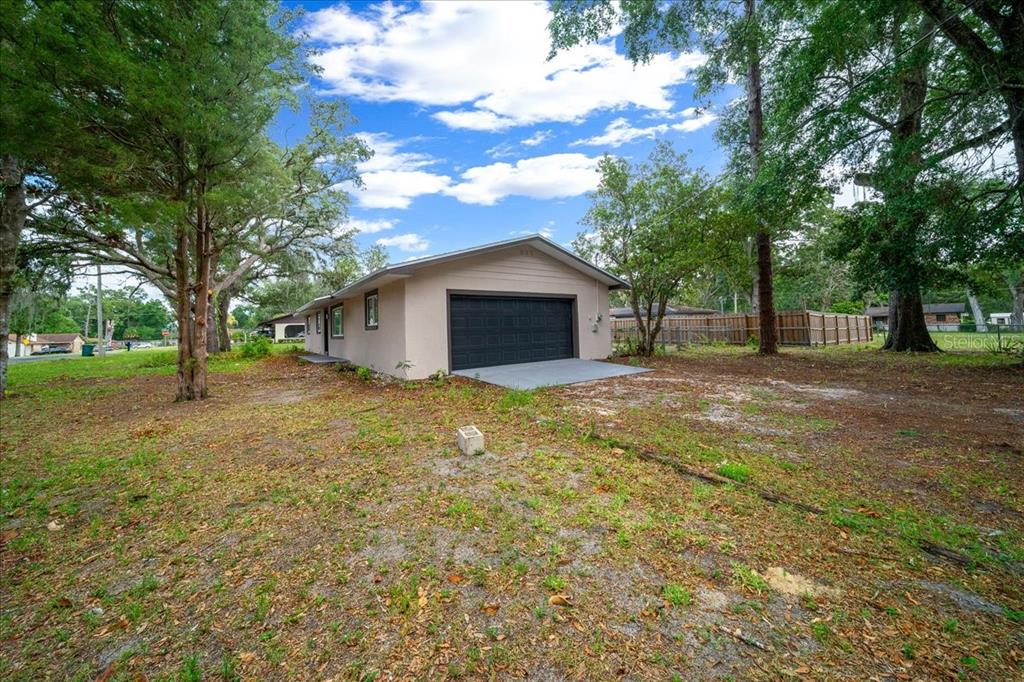 A detached garage with a black door sits on a grassy lot with mature trees — 4506 NE 10TH STREET, OCALA, FL