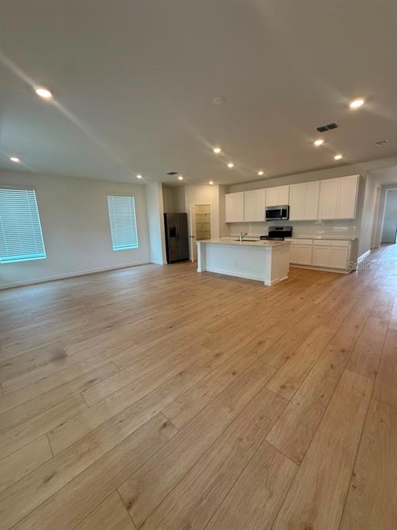 An open-concept kitchen and living area features light wood flooring and white cabinetry — 5133 ARROWFEATHER COURT, ST CLOUD, FL