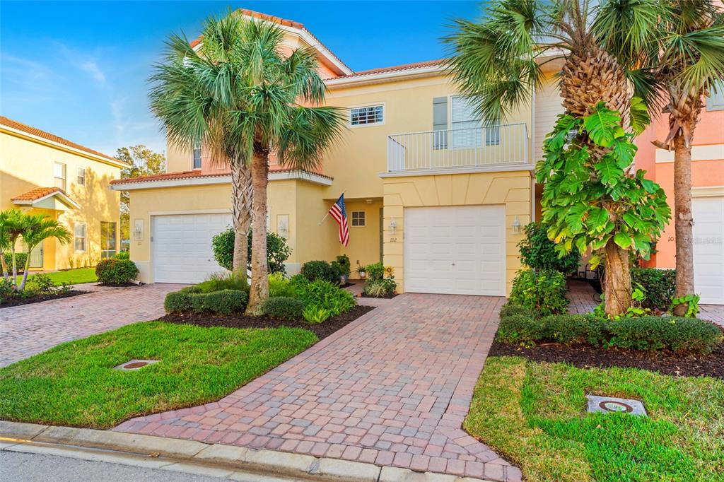 A two-story yellow townhouse with a brick driveway, two garage doors, and palm trees — 16150 VIA SOLERA CIRCLE UNIT 102, FORT MYERS, FL