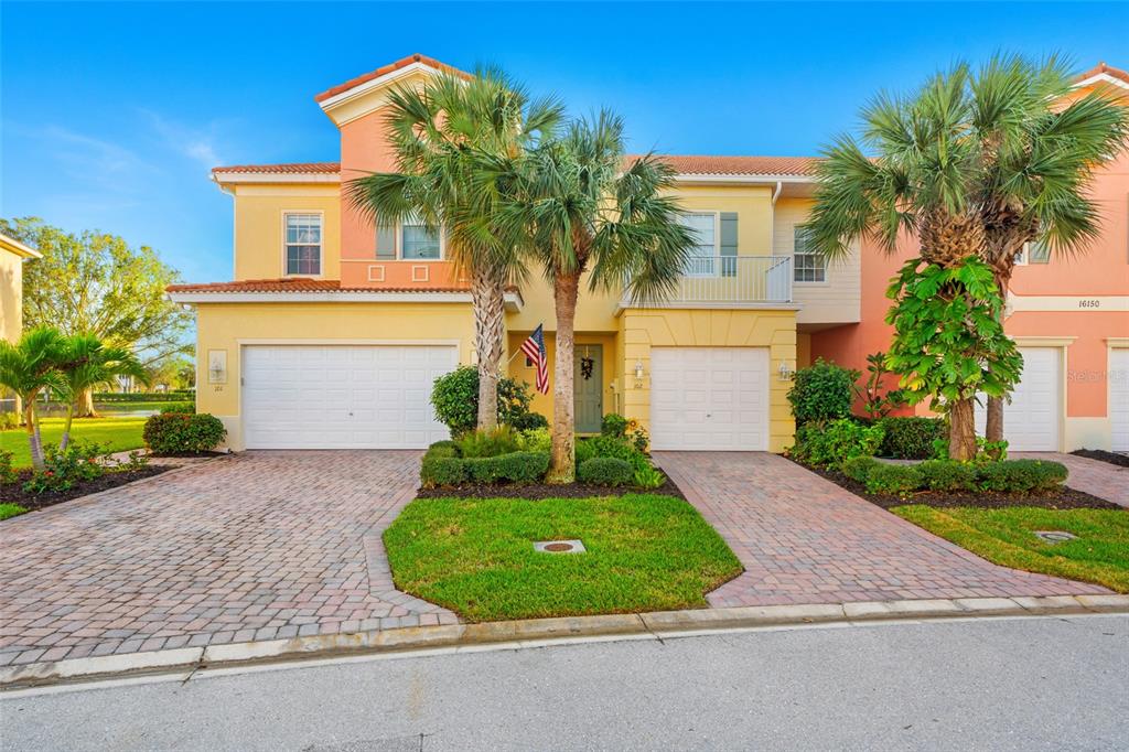 A two-story townhouse with a brick driveway, two garage doors, and palm trees in front — 16150 VIA SOLERA CIRCLE UNIT 102, FORT MYERS, FL