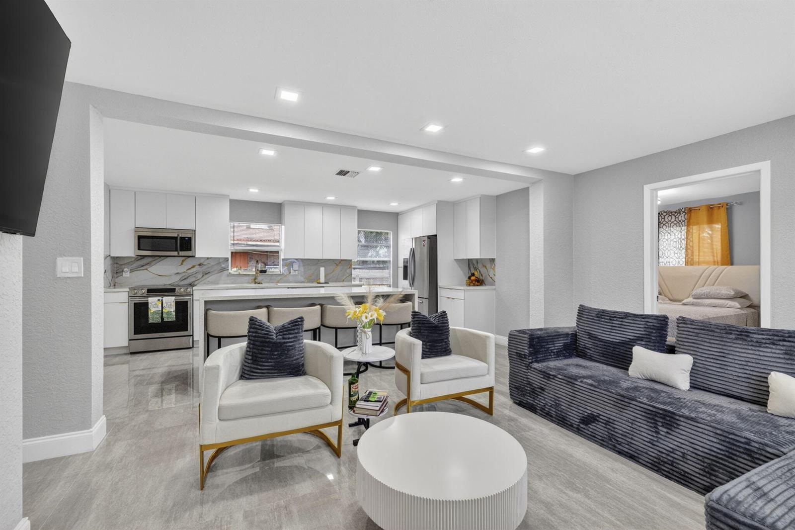 An open-concept living room and kitchen featuring gray tile floors, white cabinetry, and modern furniture — 800 NW 6th Avenue, Pompano Beach FL 33060, POMPANO BEACH, FL