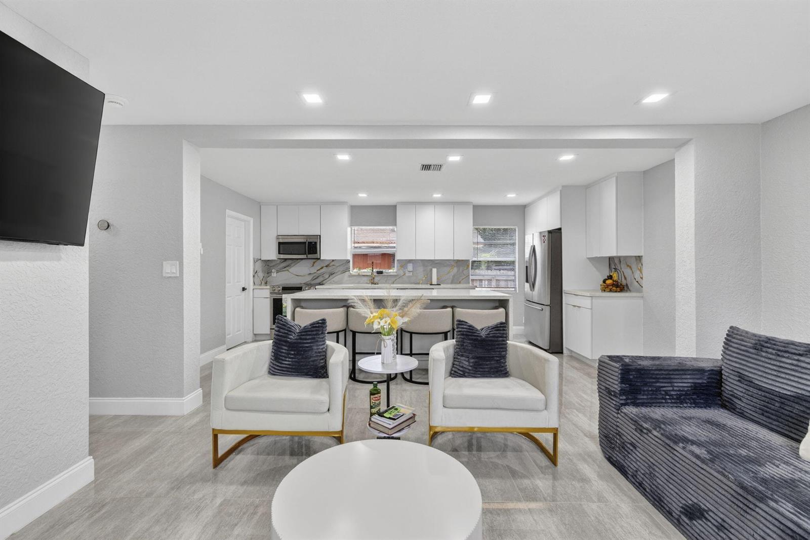 A modern open-concept kitchen features white cabinetry, marble-style backsplashes, and a central island with seating — 800 NW 6th Avenue, Pompano Beach FL 33060, POMPANO BEACH, FL