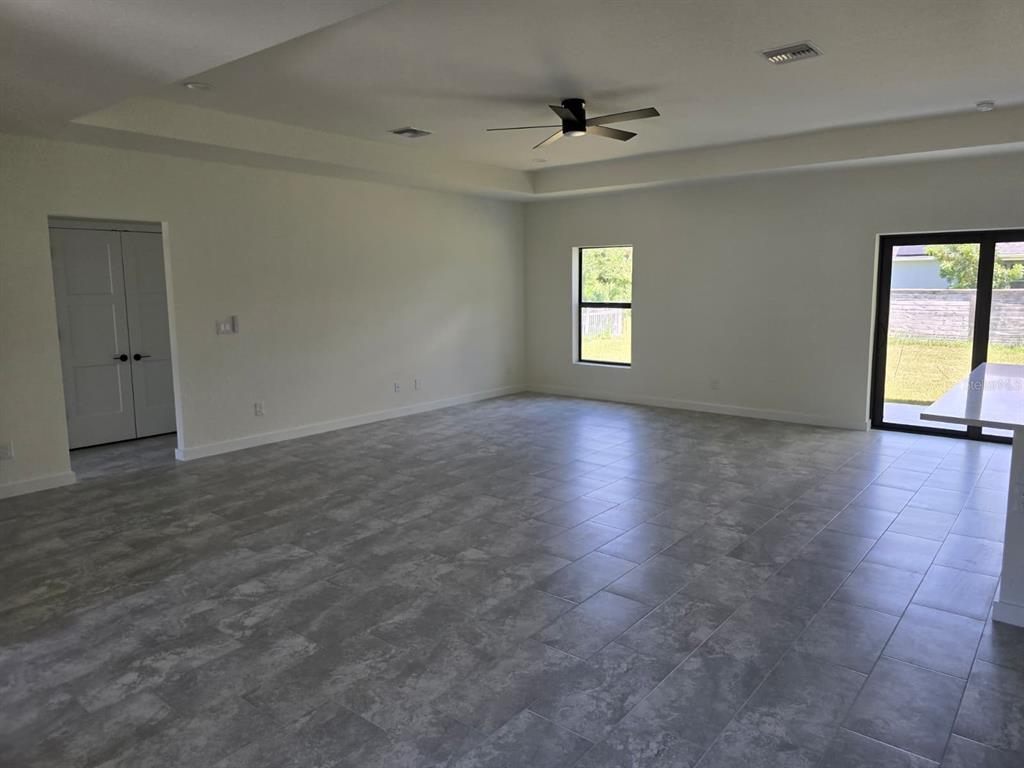 A spacious, empty room features gray tile flooring, white walls, a ceiling fan, and sliding doors — 4240 LAS ALMANOS AVENUE, NORTH PORT, FL