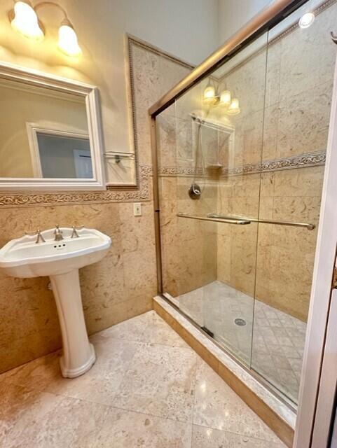 A bathroom features a pedestal sink, a glass-enclosed shower, and beige stone tile walls — 3021 Florida Boulevard, Delray Beach FL 33483, DELRAY BEACH, FL