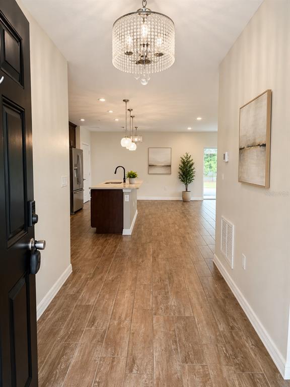 An entryway leads into an open-concept kitchen with wood-look tile flooring and a crystal chandelier — 433 SARDINIA CIRCLE, DAVENPORT, FL