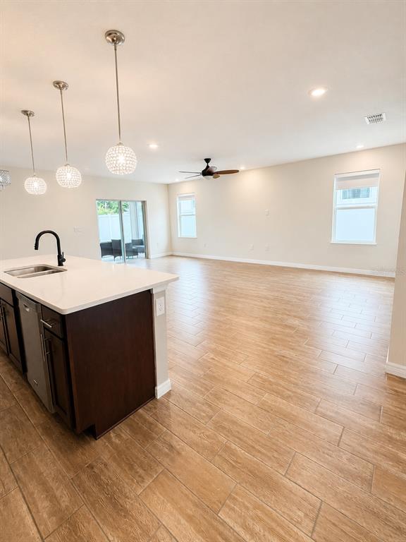 A kitchen island with a sink overlooks an open-concept living area with wood-look tile flooring — 433 SARDINIA CIRCLE, DAVENPORT, FL