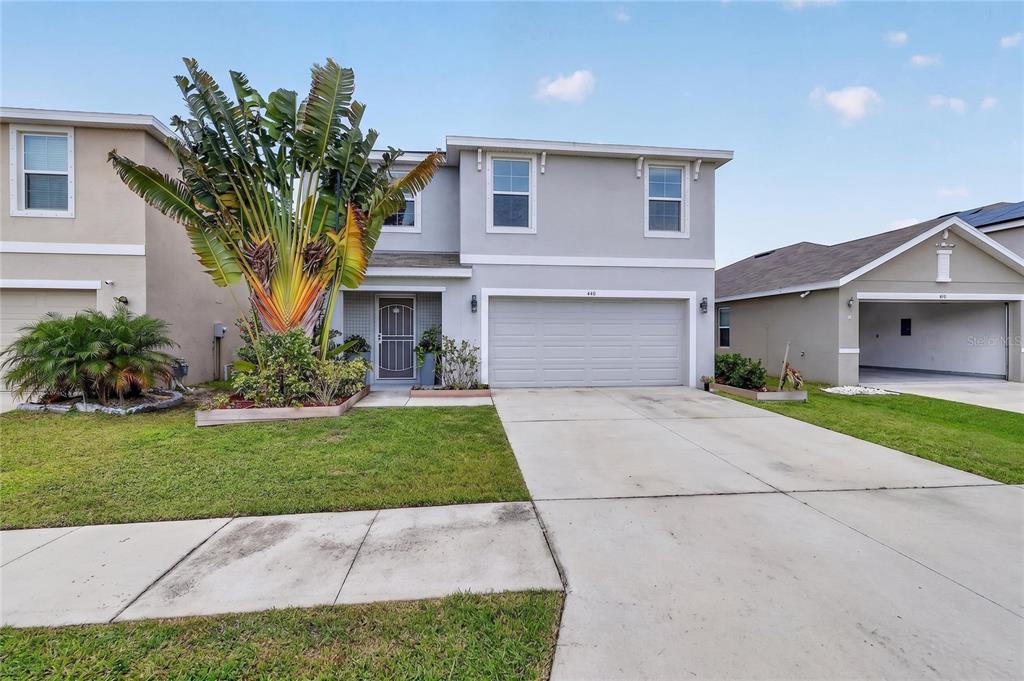 A two-story house with a gray exterior, a two-car garage, and a large tropical plant — 440 OLIVE CONCH STREET, RUSKIN, FL