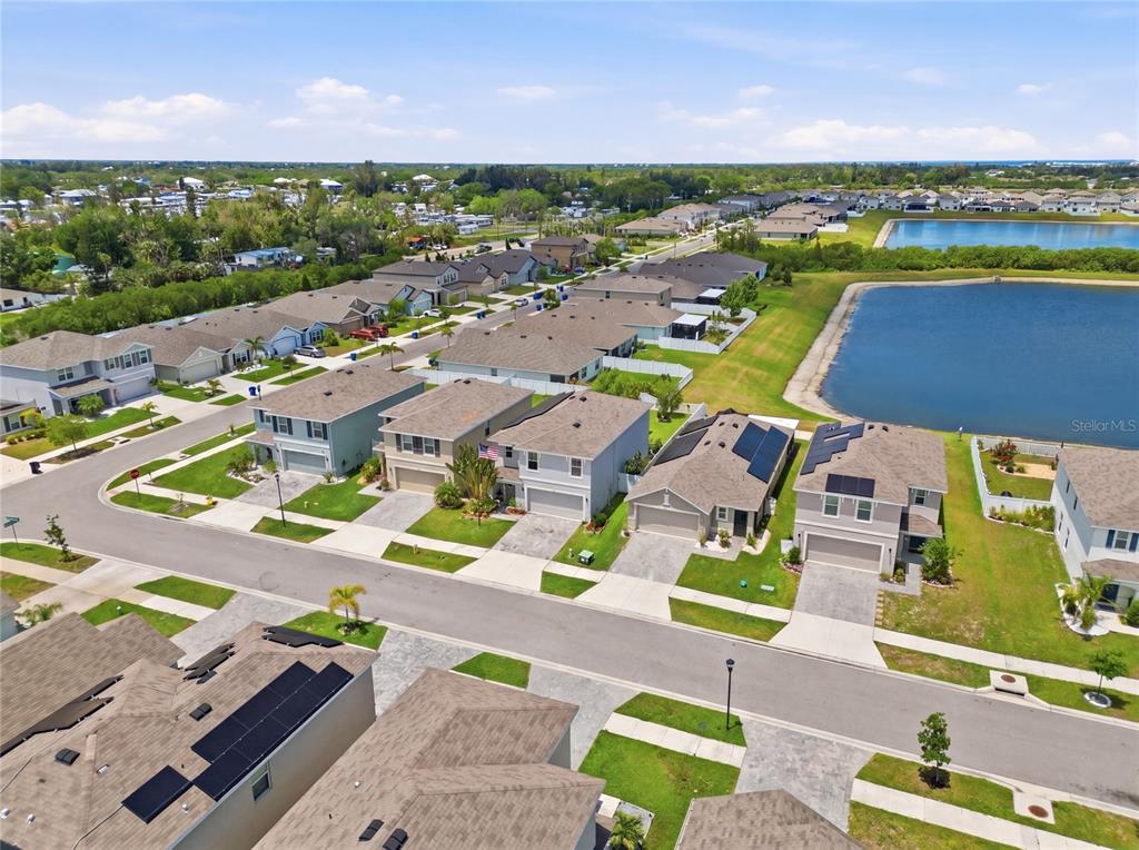 An aerial view shows a suburban neighborhood with houses, paved streets, and a large pond — 440 OLIVE CONCH STREET, RUSKIN, FL