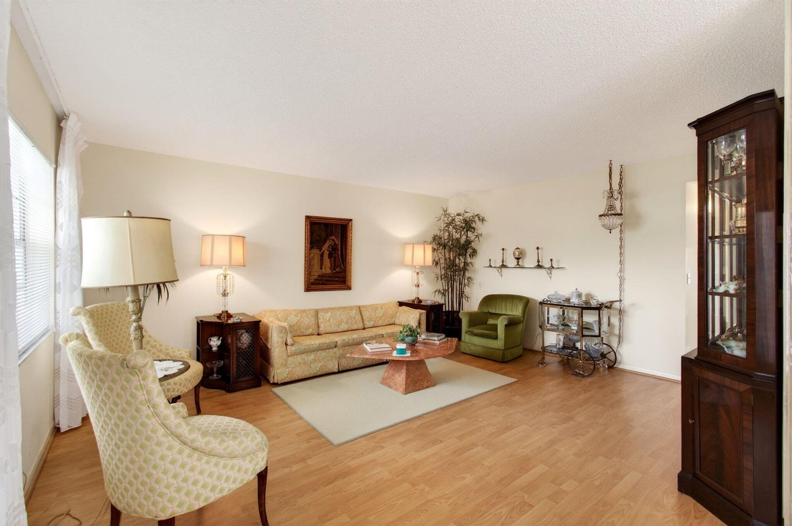 A living room features light wood flooring, a patterned sofa, two armchairs, and a display cabinet — 349 Capri # H, Delray Beach FL 33484, DELRAY BEACH, FL