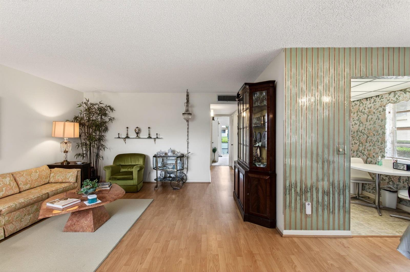 A living room with wood flooring, a floral sofa, a green armchair, and a china cabinet — 349 Capri # H, Delray Beach FL 33484, DELRAY BEACH, FL