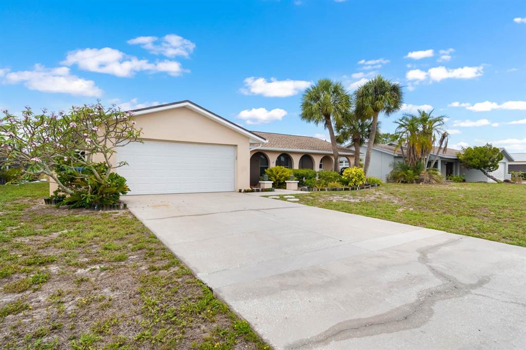 A single-story house with a white garage, arched entryway, and palm trees under a blue sky — 736 FLAMINGO DRIVE, APOLLO BEACH, FL