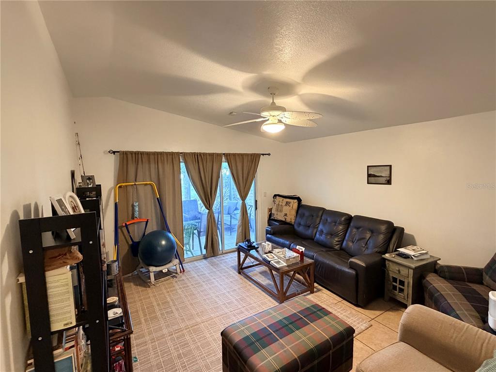 A living room features a vaulted ceiling, a ceiling fan, tile floors, and sliding glass doors — 2010 1/2 VINE STREET, LEESBURG, FL
