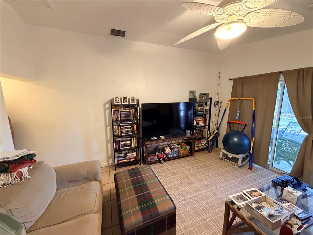 A living room features a television on a stand, bookshelves, a plaid ottoman, and sliding doors — 2010 1/2 VINE STREET, LEESBURG, FL