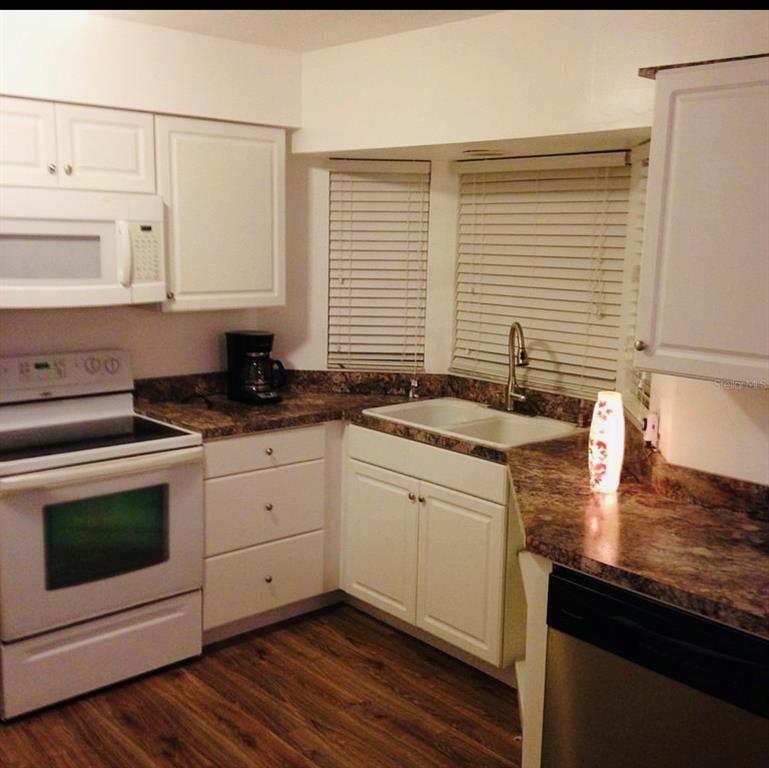 A kitchen with white cabinets, dark granite countertops, a white stove, and wood-look flooring — 2010 1/2 VINE STREET, LEESBURG, FL