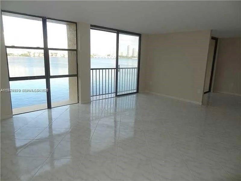A bright living room features light-colored tile floors, large windows, and a balcony overlooking water — 17500 N Bay Rd # S403, Sunny Isles Beach FL 33160, SUNNY ISLES BEACH, FL