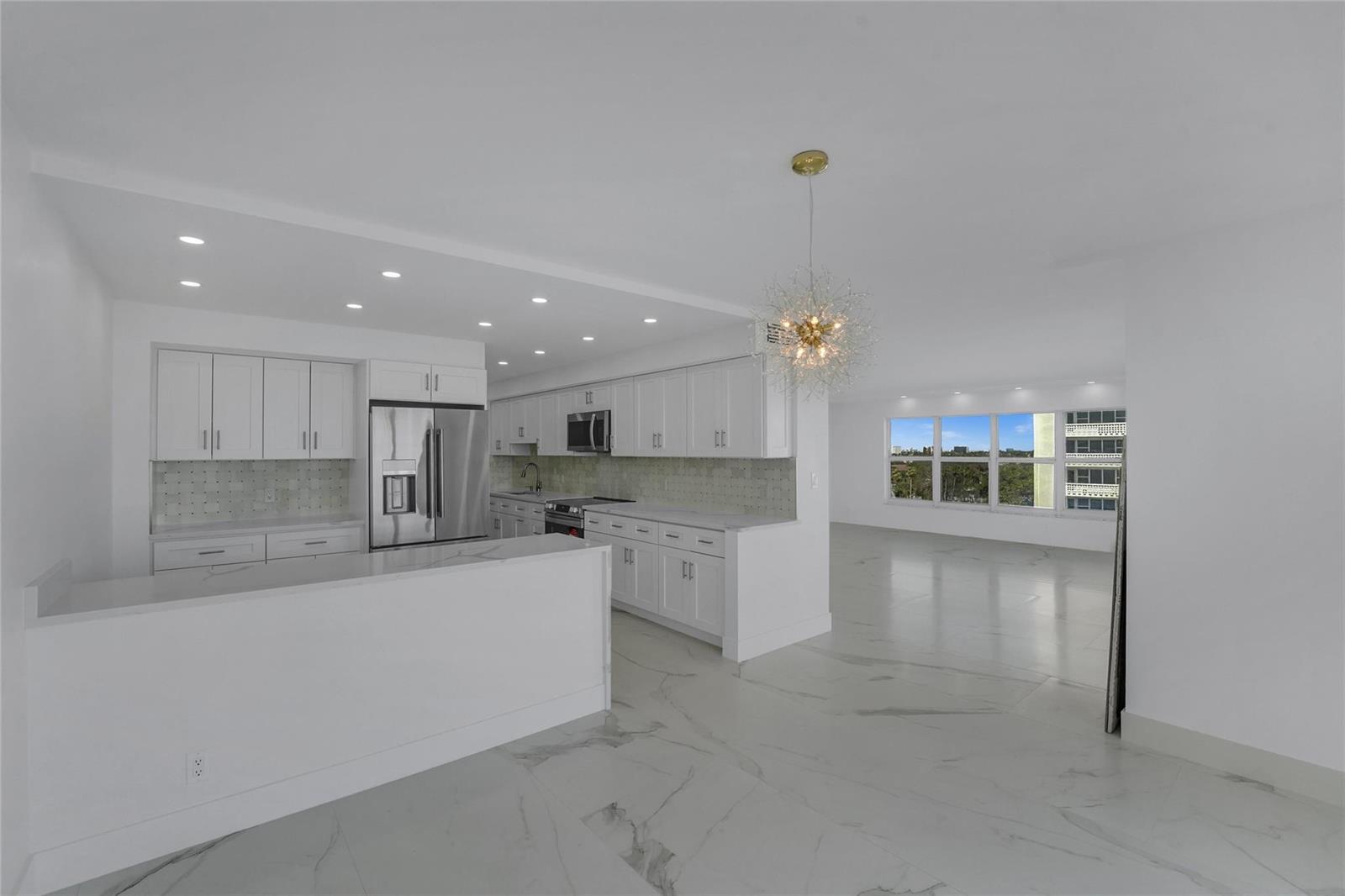 A modern white kitchen with marble-style flooring opens into a bright, empty living area — 3900 Galt Ocean Drive # 511, Fort Lauderdale FL 33308, FORT LAUDERDALE, FL