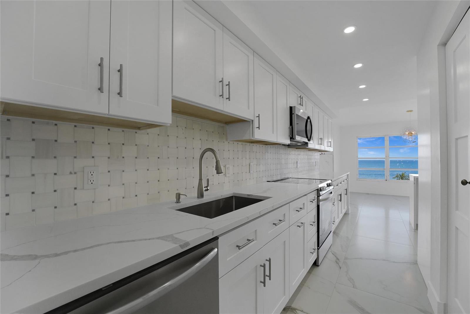A modern white kitchen features marble-style countertops, a tiled backsplash, and an ocean view — 3900 Galt Ocean Drive # 511, Fort Lauderdale FL 33308, FORT LAUDERDALE, FL