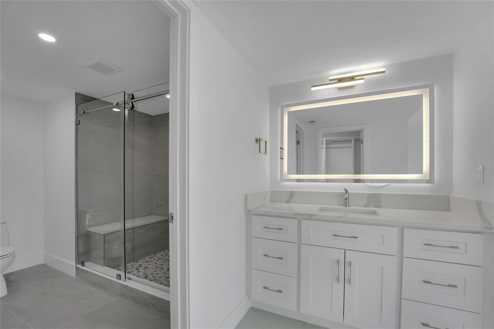 A modern bathroom features a white vanity, a backlit mirror, and a glass-enclosed walk-in shower — 3900 Galt Ocean Drive # 511, Fort Lauderdale FL 33308, FORT LAUDERDALE, FL