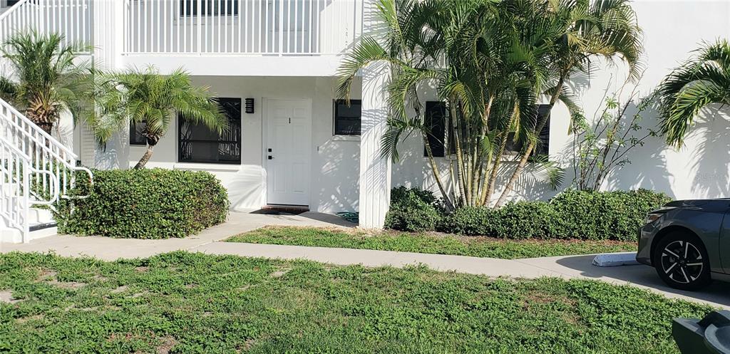 The exterior of a white multi-story building features a ground-floor entrance, landscaping, and a car — 2616 ST JOSEPHS DRIVE W UNIT 1, DUNEDIN, FL
