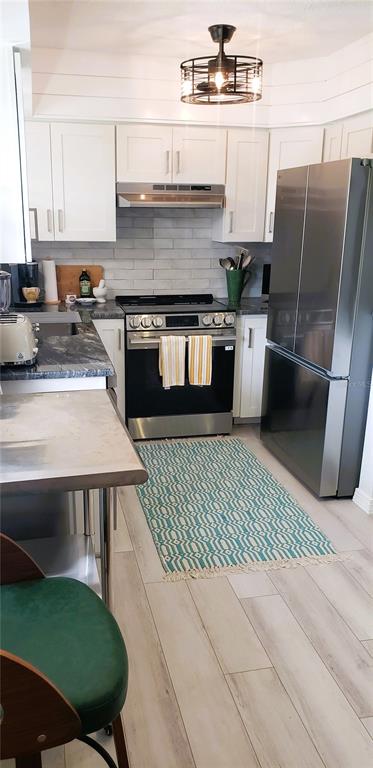 A kitchen features white cabinets, stainless steel appliances, a subway tile backsplash, and a patterned rug — 2616 ST JOSEPHS DRIVE W UNIT 1, DUNEDIN, FL