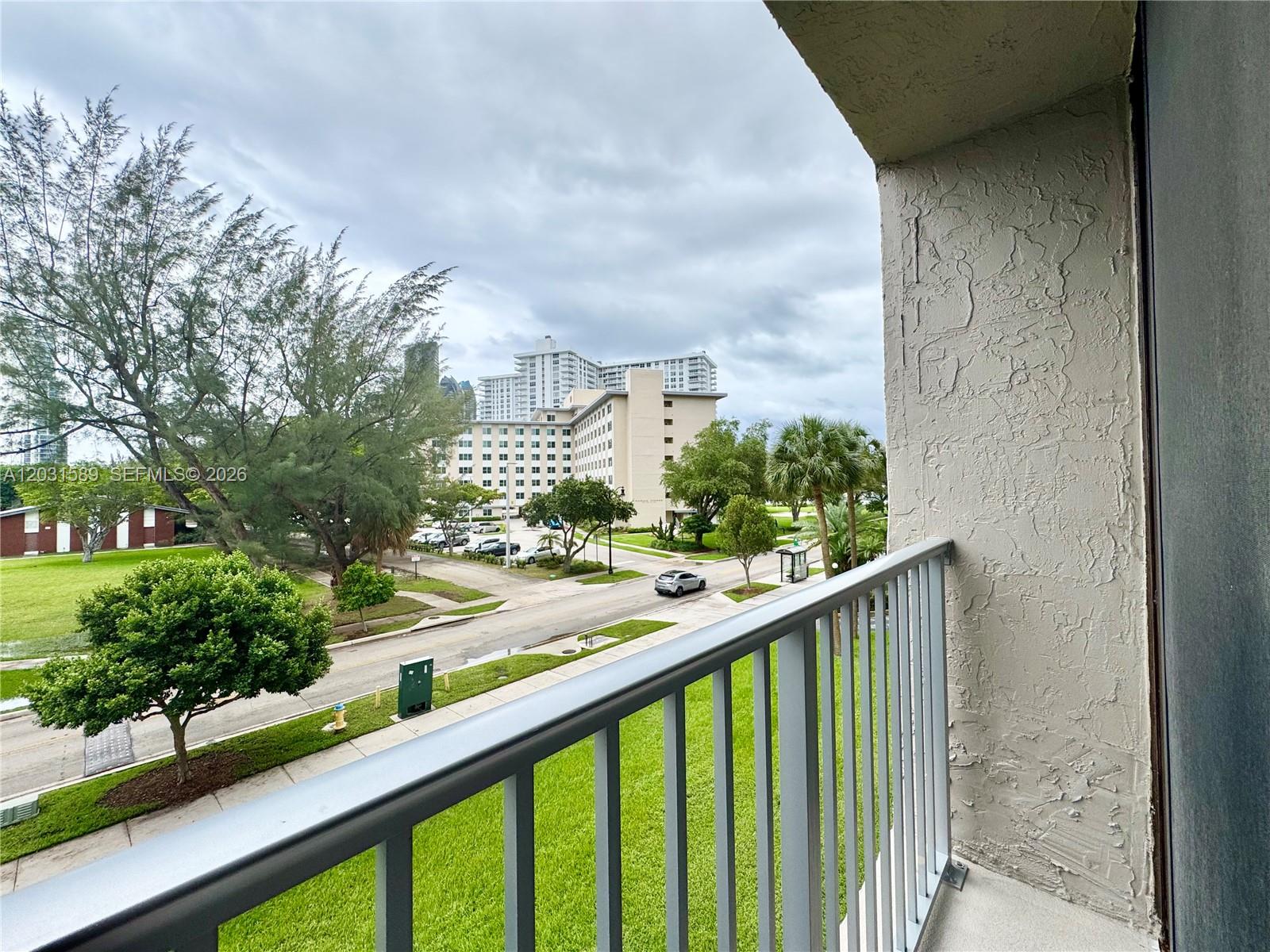 A balcony view overlooks a street, green lawns, trees, and nearby apartment buildings — 17600 N Bay Rd # N302, Sunny Isles Beach FL 33160, SUNNY ISLES BEACH, FL