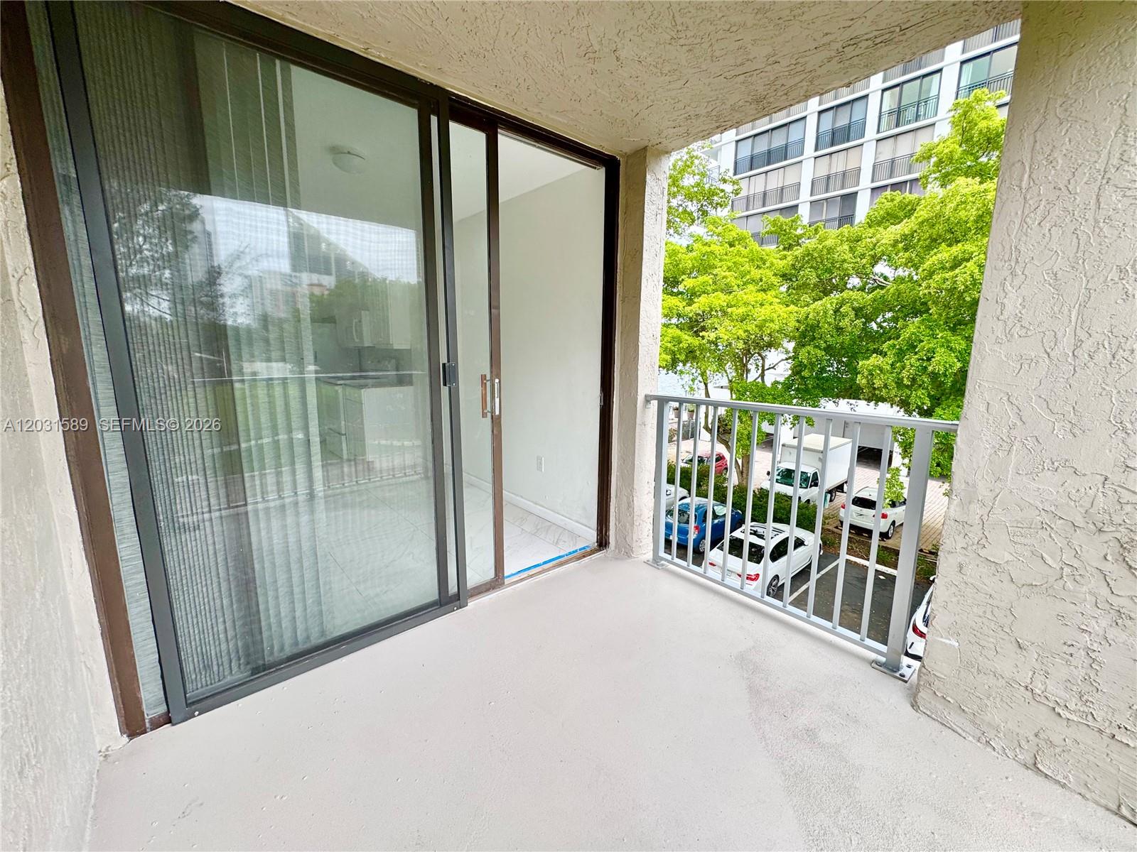 A balcony with a sliding glass door overlooks a parking lot and trees — 17600 N Bay Rd # N302, Sunny Isles Beach FL 33160, SUNNY ISLES BEACH, FL