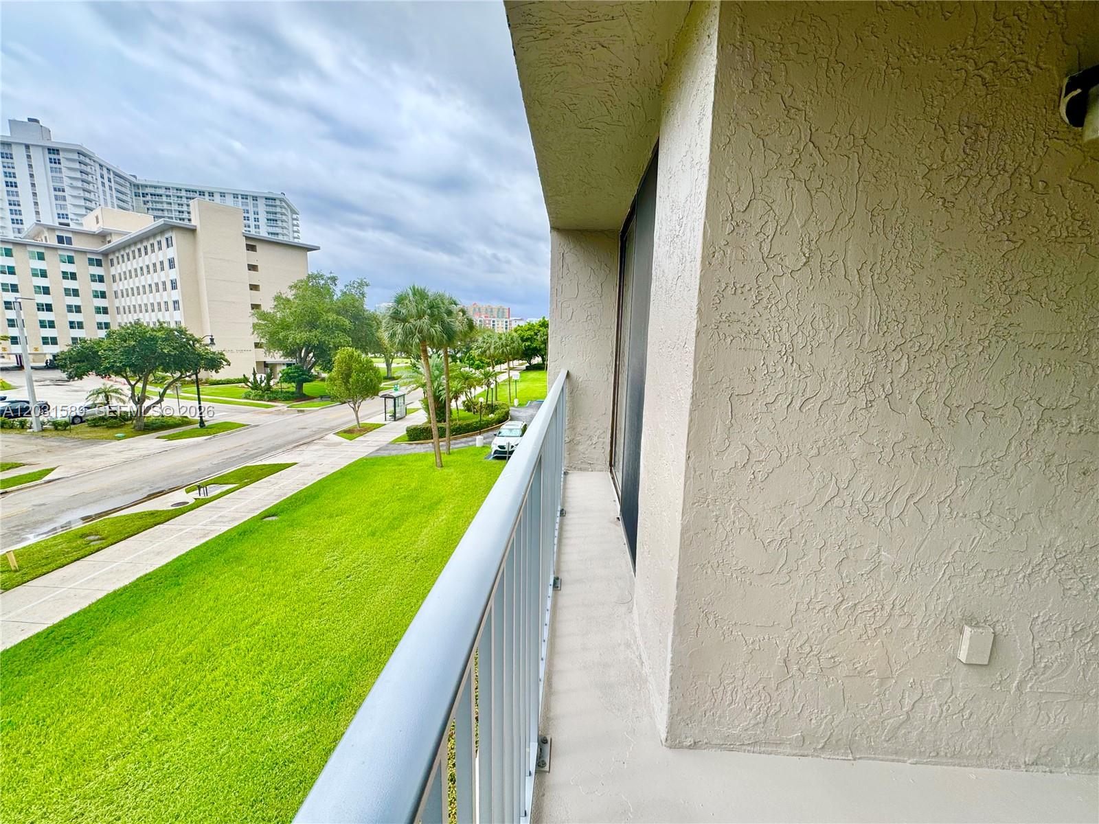 A balcony with a metal railing overlooks a grassy lawn, a street, and buildings — 17600 N Bay Rd # N302, Sunny Isles Beach FL 33160, SUNNY ISLES BEACH, FL