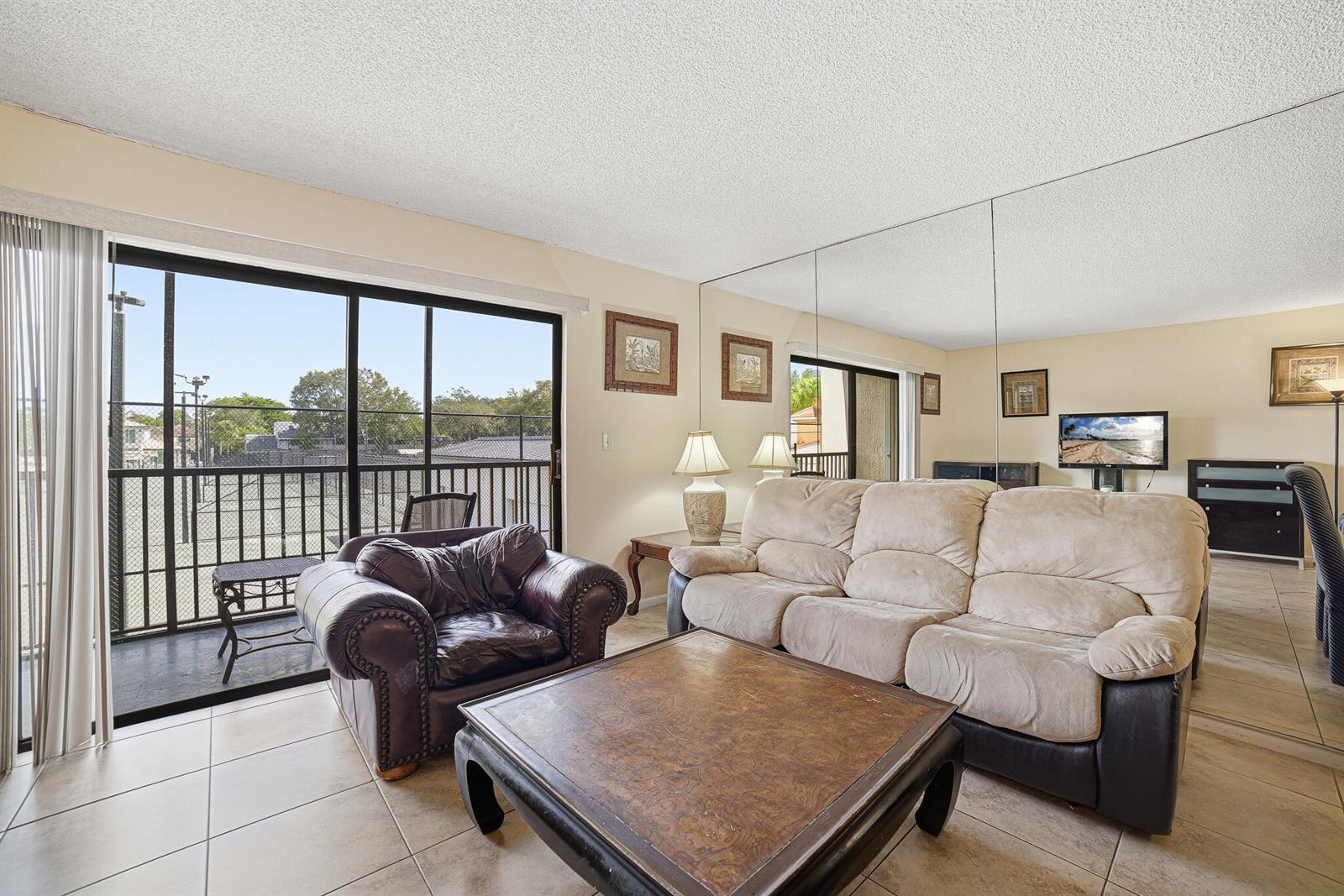 A living room features a beige sofa, a leather armchair, a coffee table, and mirrored walls — 105 Deer Creek Road # 202, Deerfield Beach FL 33442, DEERFIELD BEACH, FL