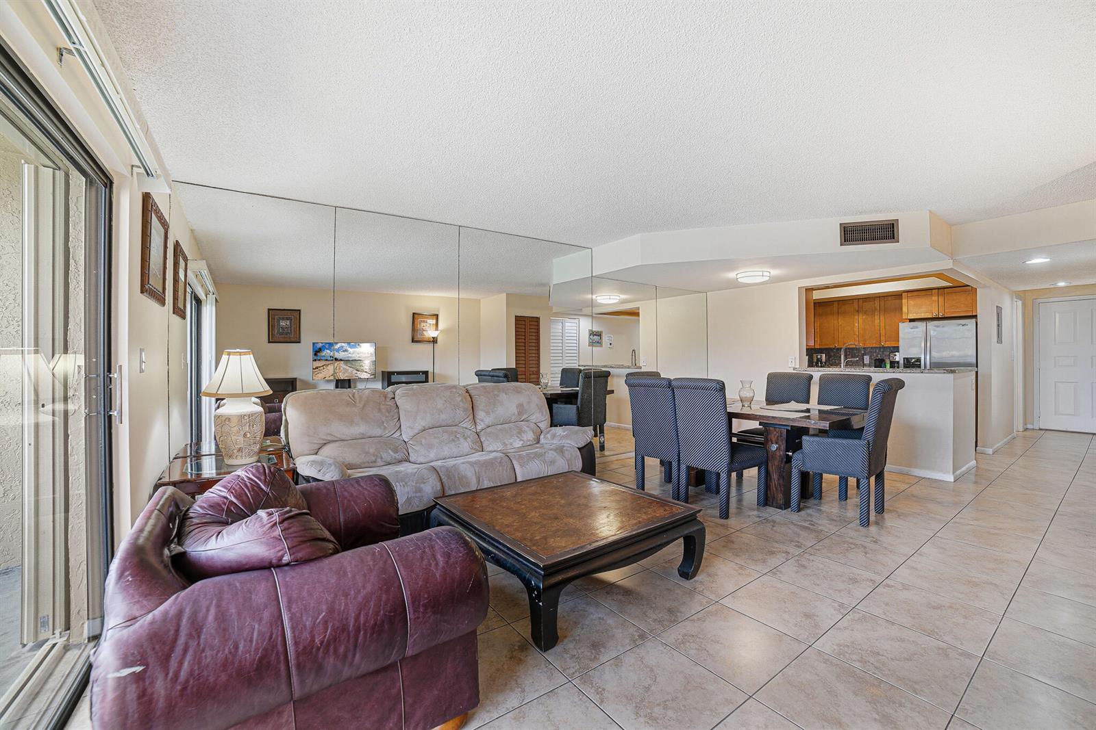 A living and dining area features tiled floors, a mirrored wall, and a kitchen pass-through — 105 Deer Creek Road # 202, Deerfield Beach FL 33442, DEERFIELD BEACH, FL