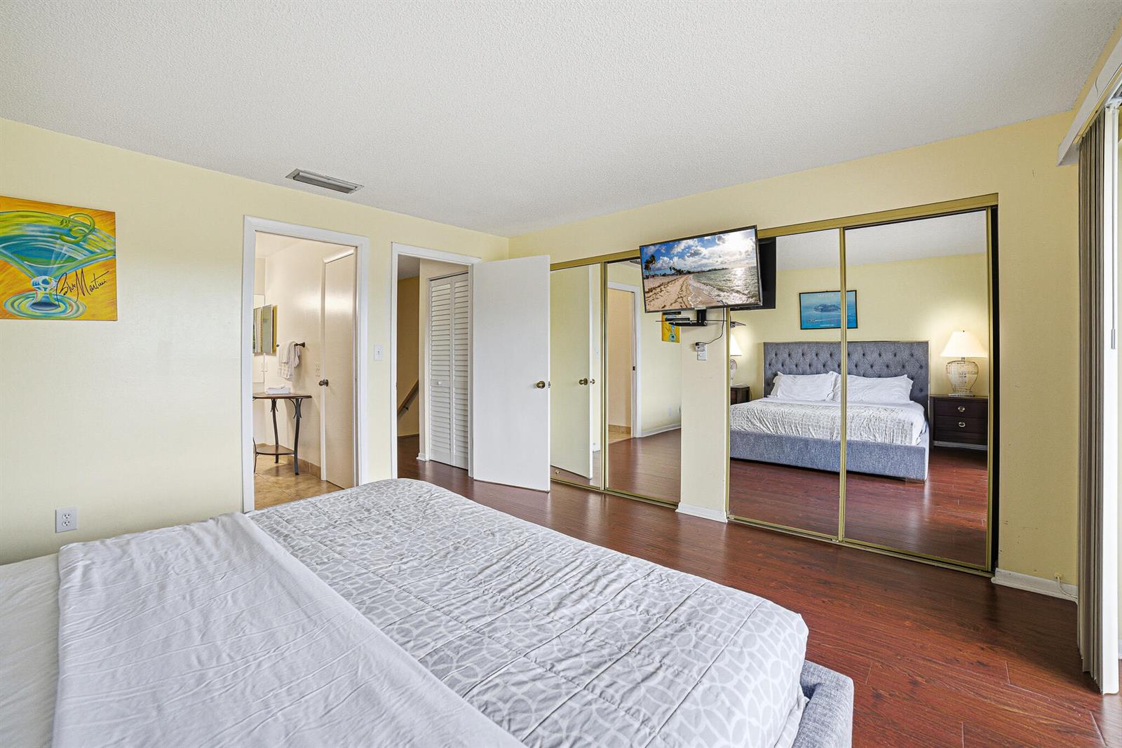 A bedroom with wood flooring, a bed, mirrored closet doors, and an attached bathroom — 105 Deer Creek Road # 202, Deerfield Beach FL 33442, DEERFIELD BEACH, FL