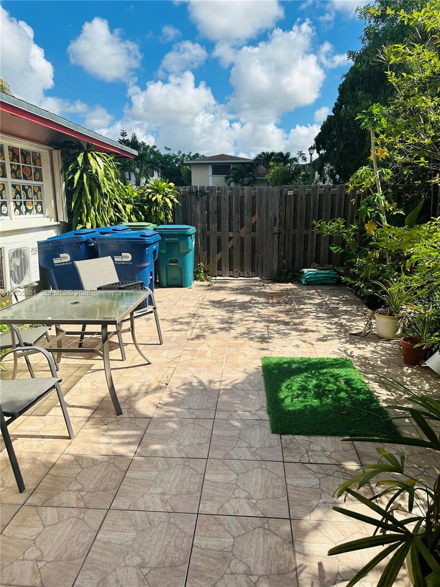 A paved outdoor patio features a dining set, trash bins, and a wooden privacy fence — MIAMI, FL